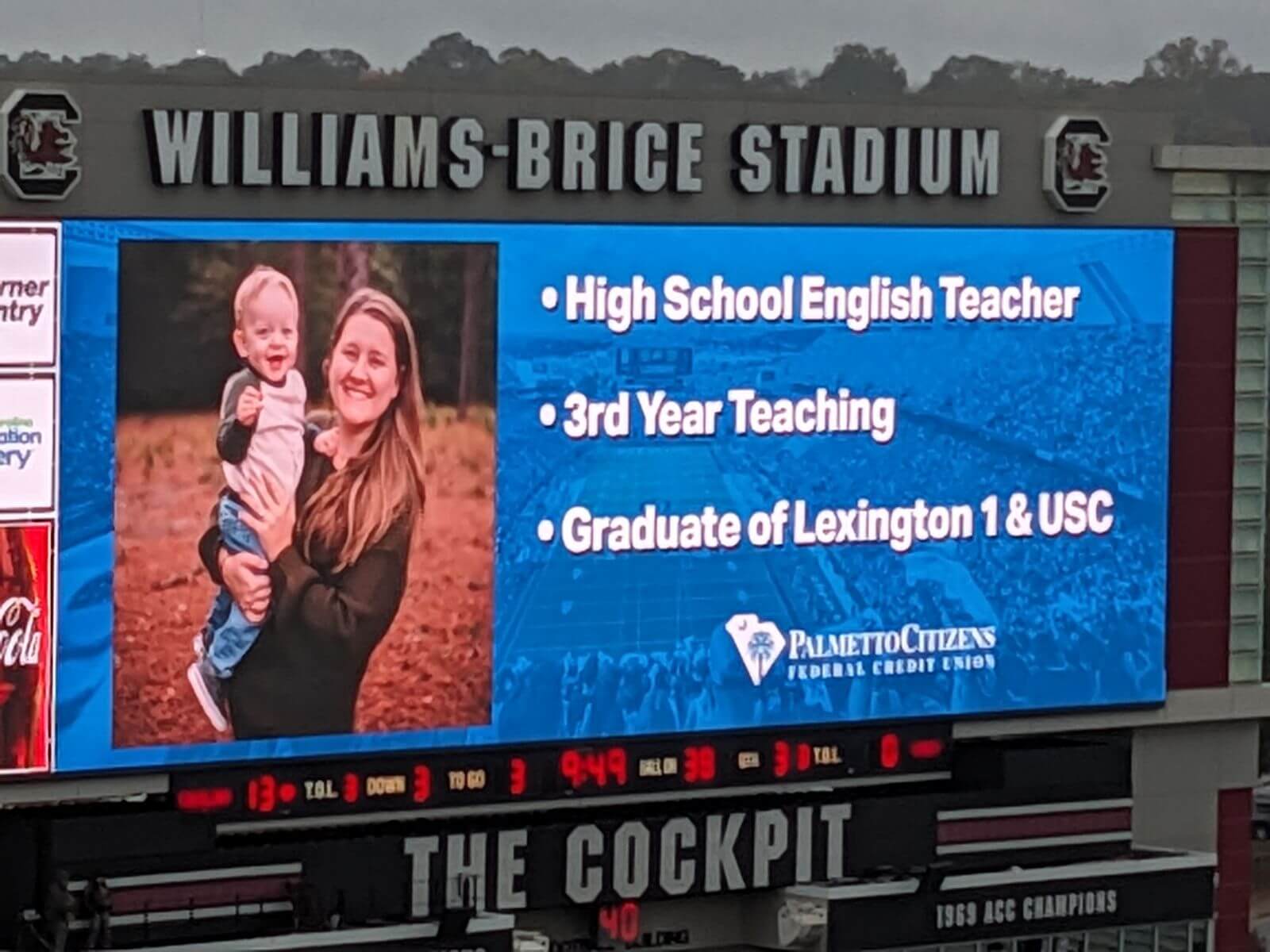 Stadium scoreboard featuring a high school English teacher and child with teaching credentials at Williams-Brice Stadium.
