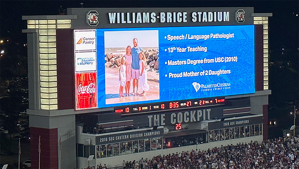 Stadium screen displaying a speech/language pathologist's achievements with a family photo at Williams-Brice Stadium.