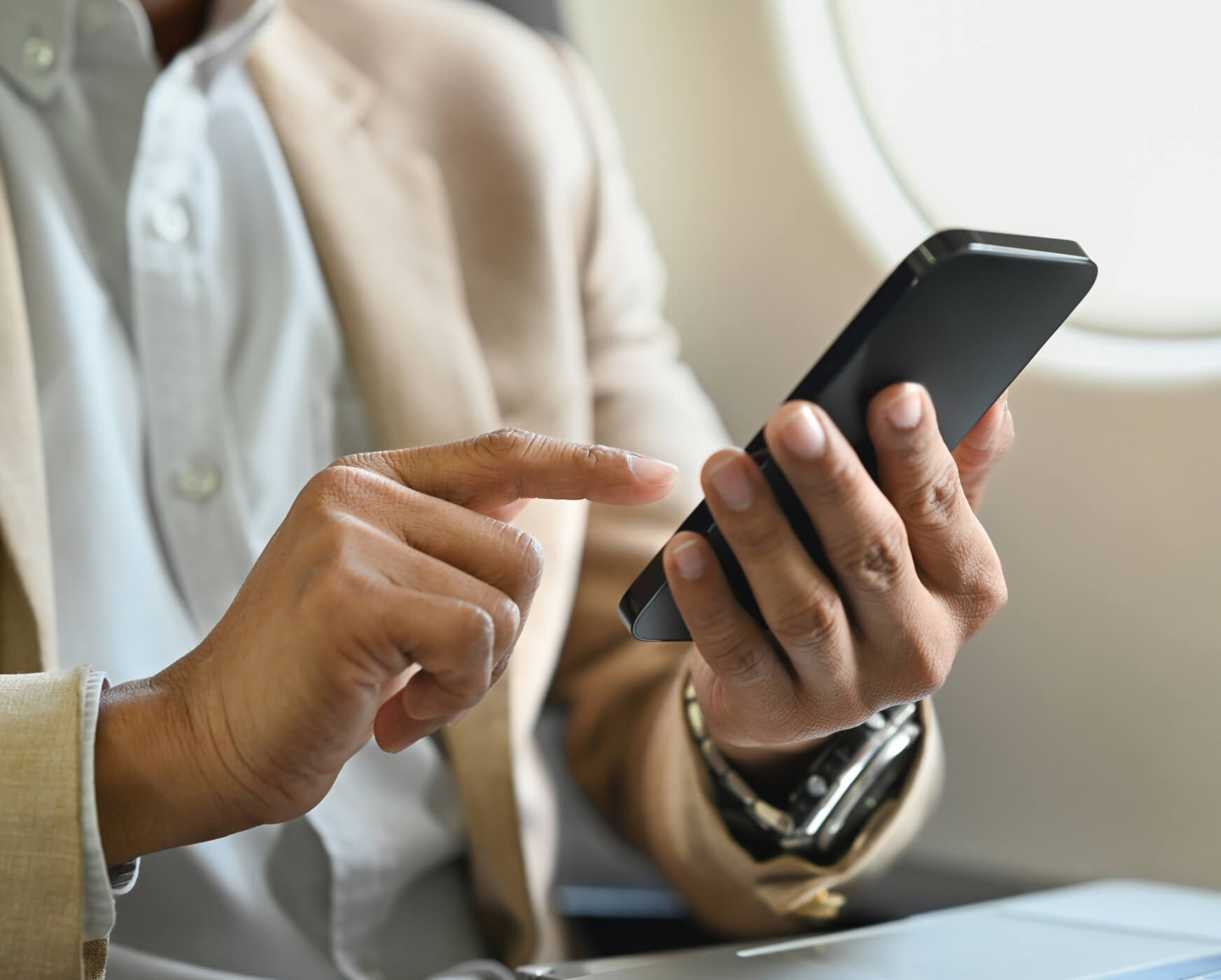 Close-up of hands using a smartphone, stylish attire, onboard an aircraft.