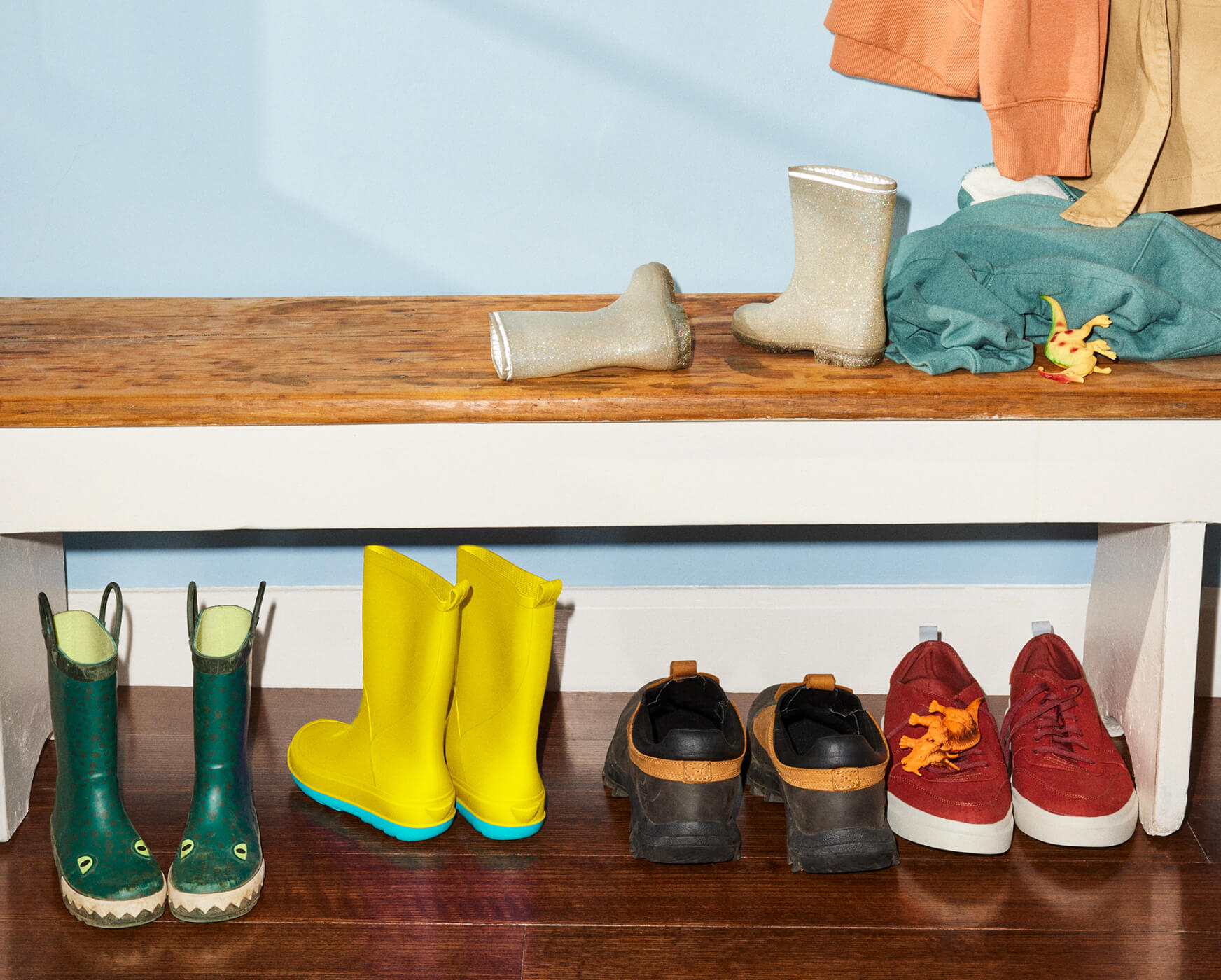 A home entryway with coats hung on the wall and shoes beneath a bench.