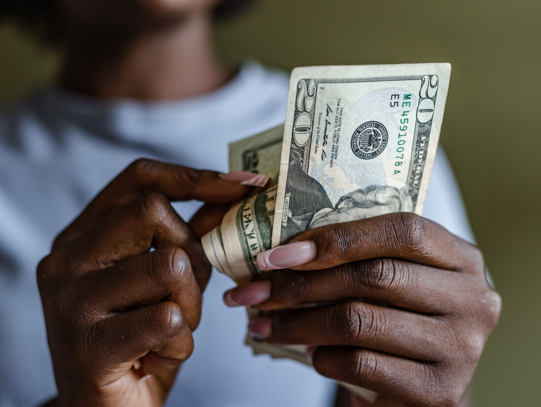 Hands counting a stack of US dollar bills.